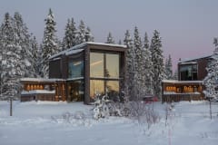 Several Jänkä villas set among snow-covered forest scenery, with warm interior lights contrasting the winter landscape.