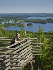 Woman on a lookout tower with lake and forest view.