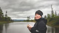 Retkeilijä kuksa kädessään lammen rannalla. Taustalla pilvinen taivas. / A hiker with a cup in his hand on the shore of a pond. Cloudy sky in the background. Kuva: Heikki Sulander.