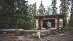 Retkeilijä laavulla kesäisessä luonnossa. Taustalla vanhaa kuusimetsää. / A hiker on a log building in the summer. An old spruce forest in the background. Kuva:Heikki Sulander