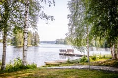 There is a rowing boat by the lake shore as well as a jetty and some birch trees.