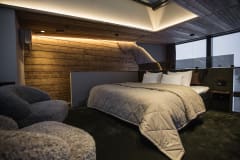 A softly lit villa bedroom at Jänkä with a large bed, wooden wall panels, warm textiles, and a peaceful view through a large window.