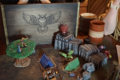 A tabletop battle map containing miniature tents, wagons and other terrain pieces