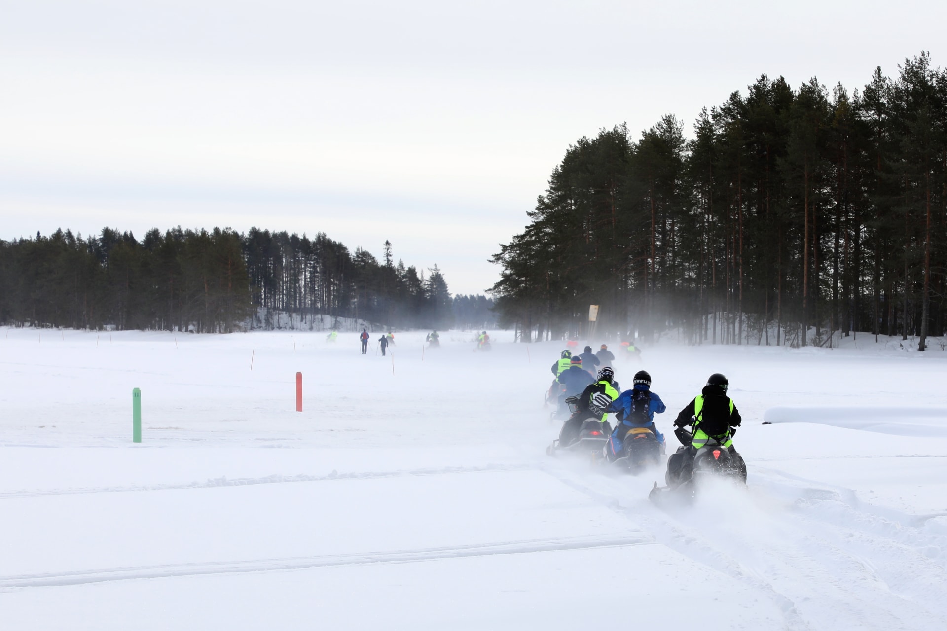 A snowmobile safari speeds over lake ice, kicking up snow crystal clouds into the air.