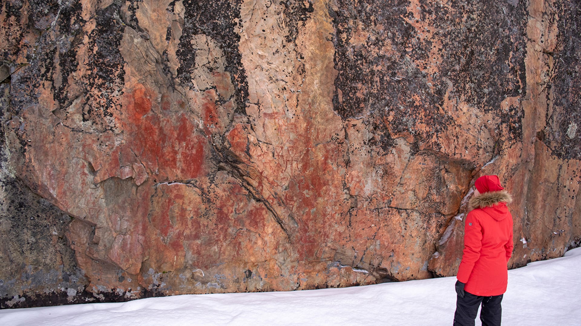 Retkeilijä katselee pystysuorassa kallioseinämässä olevia kalliomaalauksia. / A hiker looks at rock paintings on a vertical rock face. Kuva: Sirke Seppänen