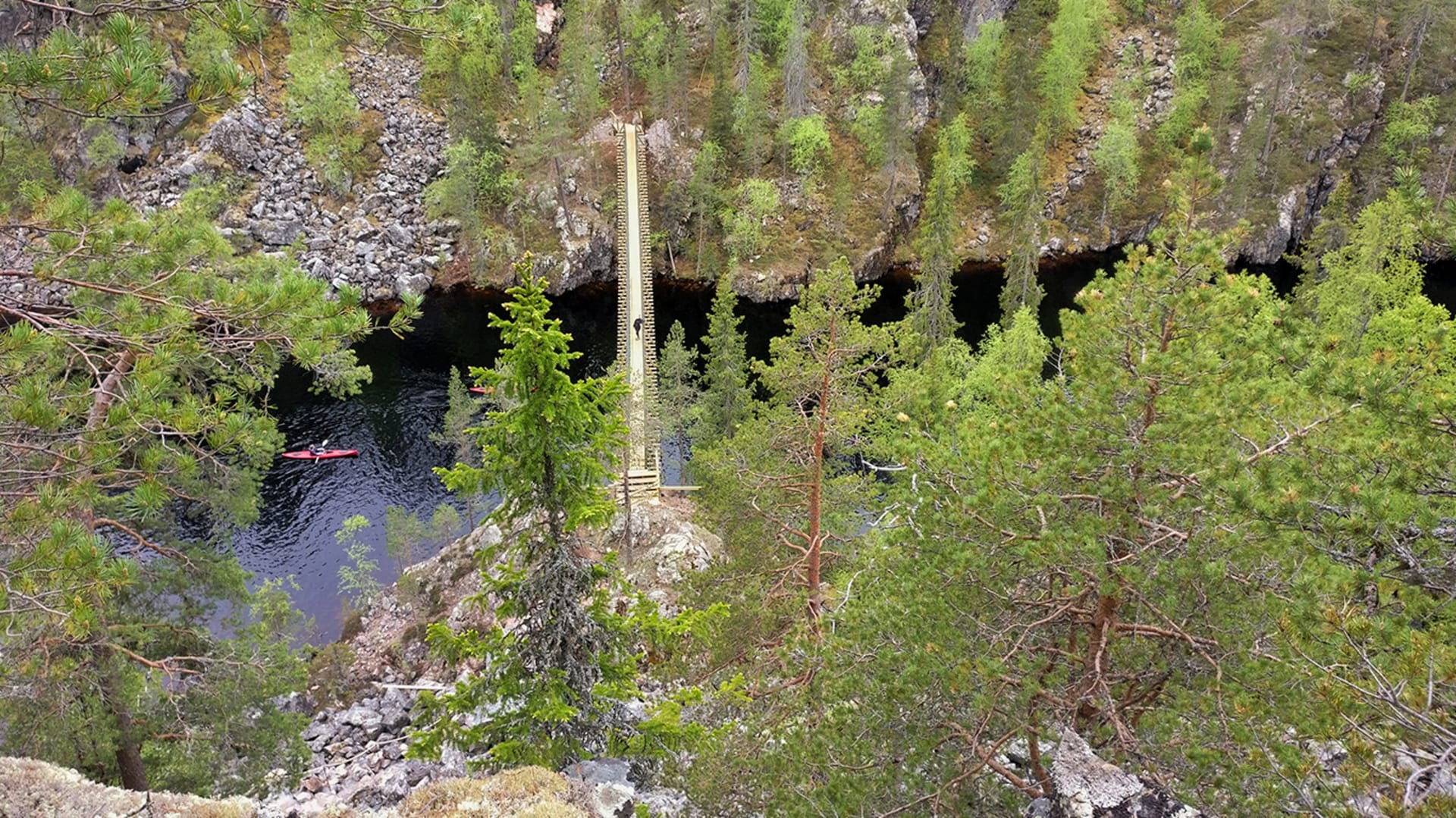 Kesäinen maisema Julma-Ölkyn kanjonista Hossan kansallispuistosta. Kallioisen kanjonin läpi kulkee riippusilta, kanjonin pohjalla järvi. Kuva: Elina Odé