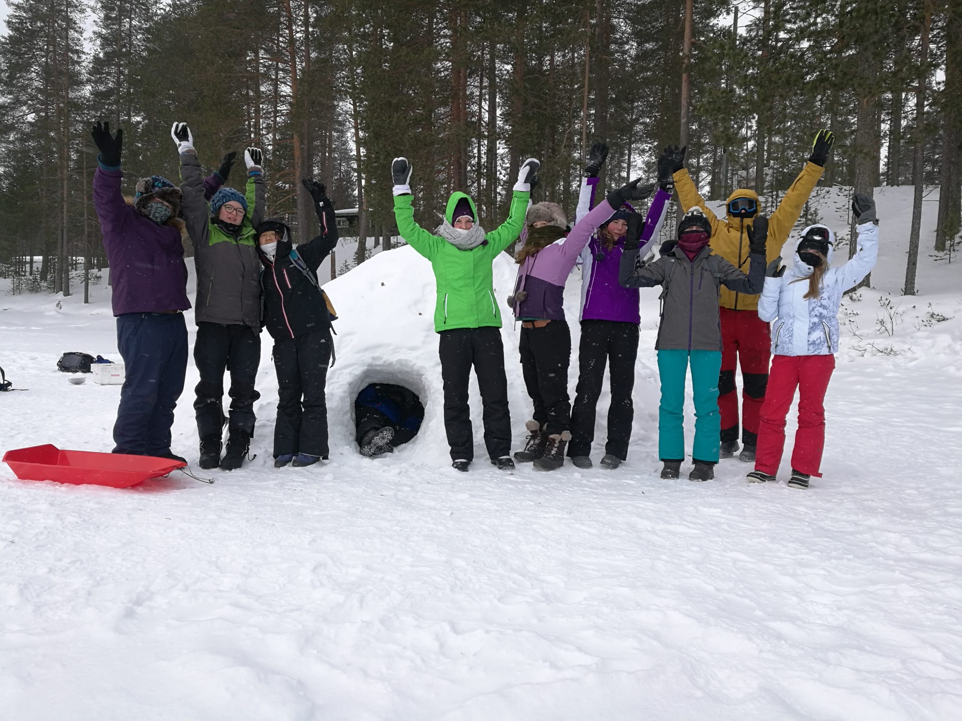 A group of children waving in front of and igloo they have made