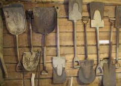 In the picture, there are various shovels on the museum wall.