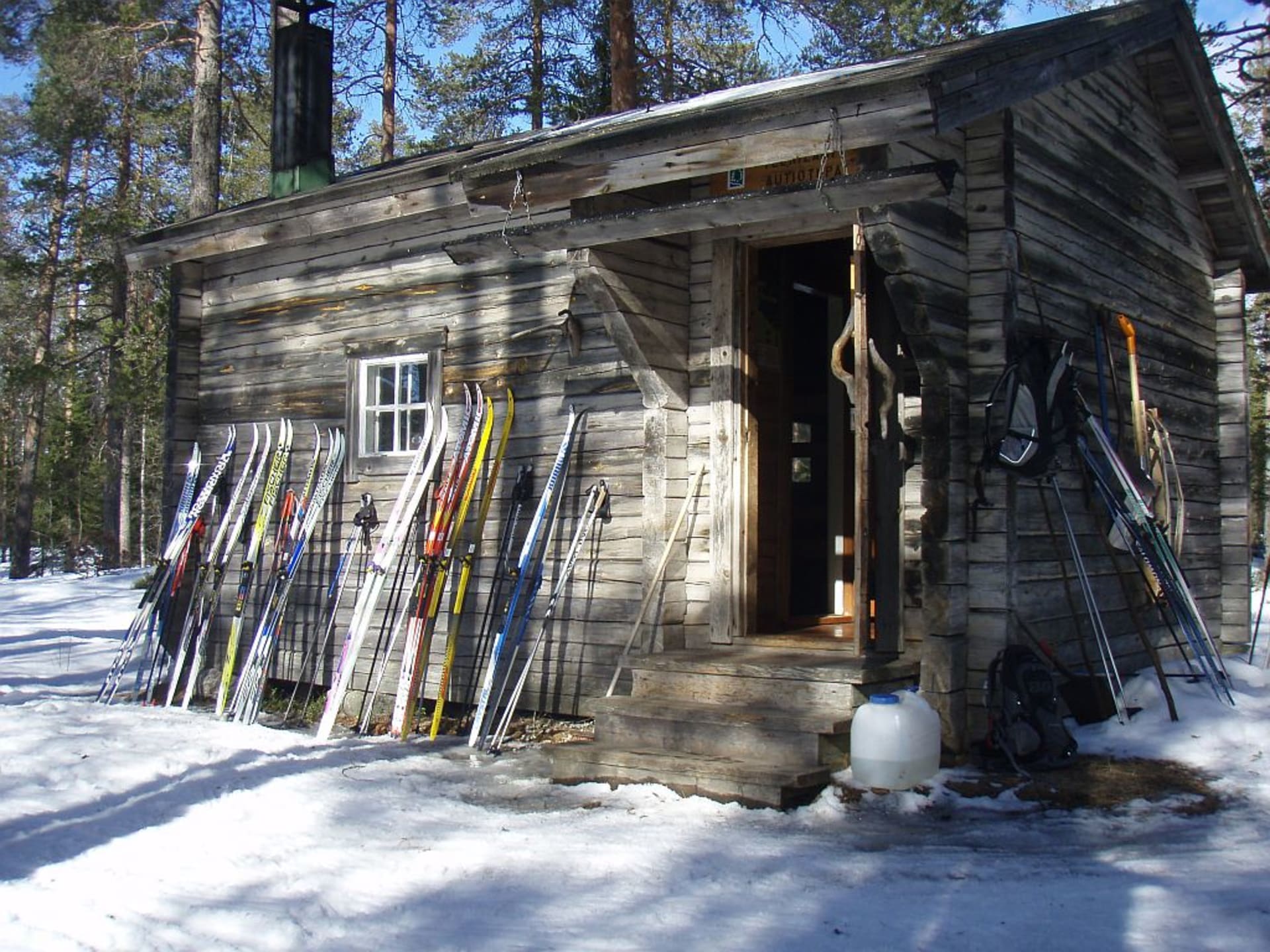 A wooden wilderness hut with a lot of skis lying against the wall