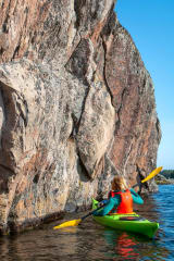 A person kayaking next to the old rock paintings.