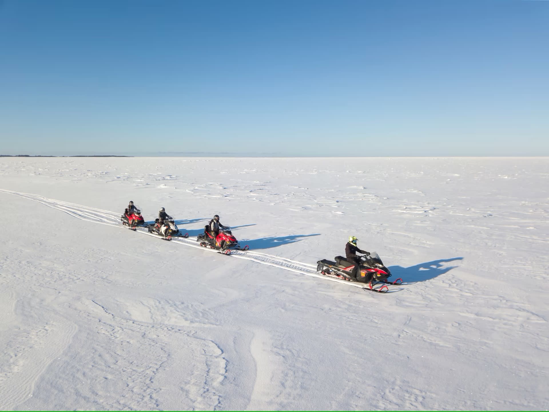 Sledders driving snowmobiles on ice.