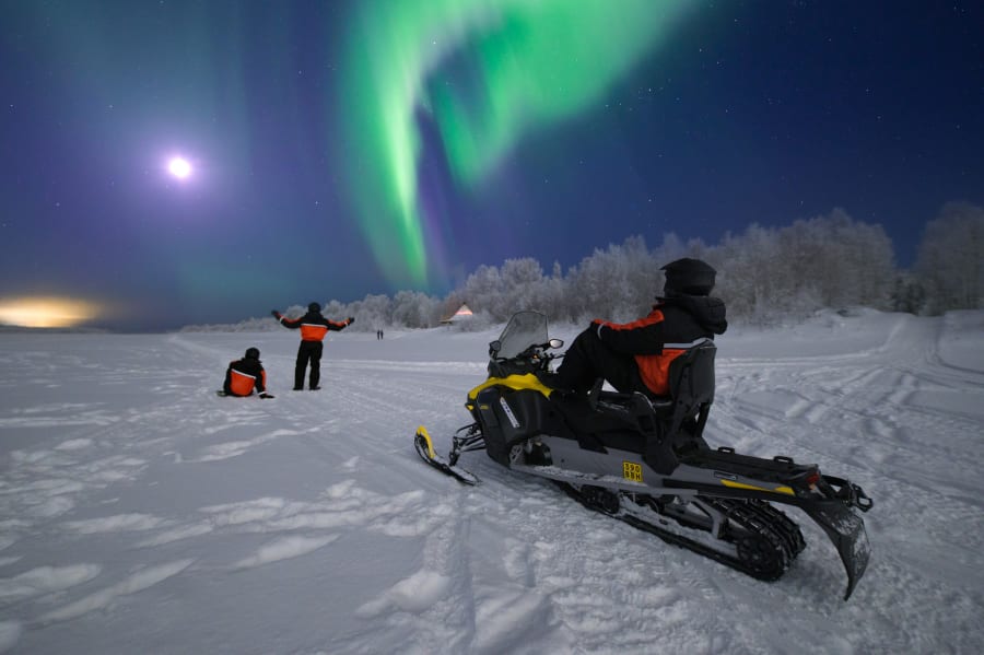 Three friends look at the Northern lights after a Snowmobile tour