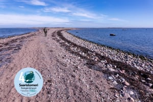 Sorasta muodostuvan kannaksen molemmin puolin on merta. Kannaksella kävelee mies.On both sides of the isthmus formed by gravel is the sea. A man is walking on the isthmus.
