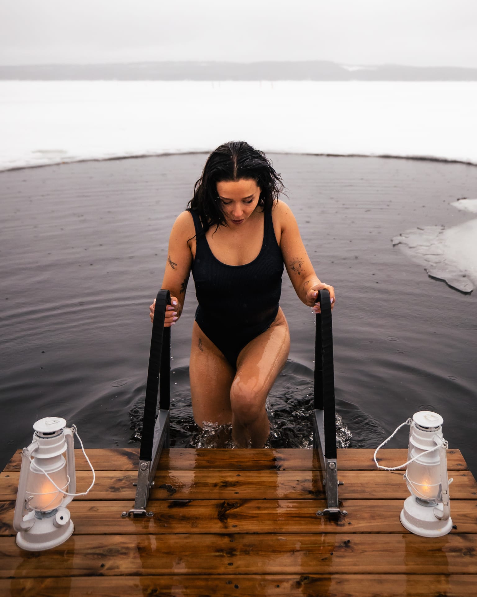 A woman emerging from a ice plunge in snowy lake setting.
