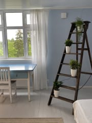 Vaaleansinisessä huoneessa vanha pöytä ja tuoli sekä tikkaat ja viherkasveja