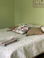 Vaaleanvihreässä huoneessa parisänky, jonka päällä päiväpeitto ja koristetyynyjä