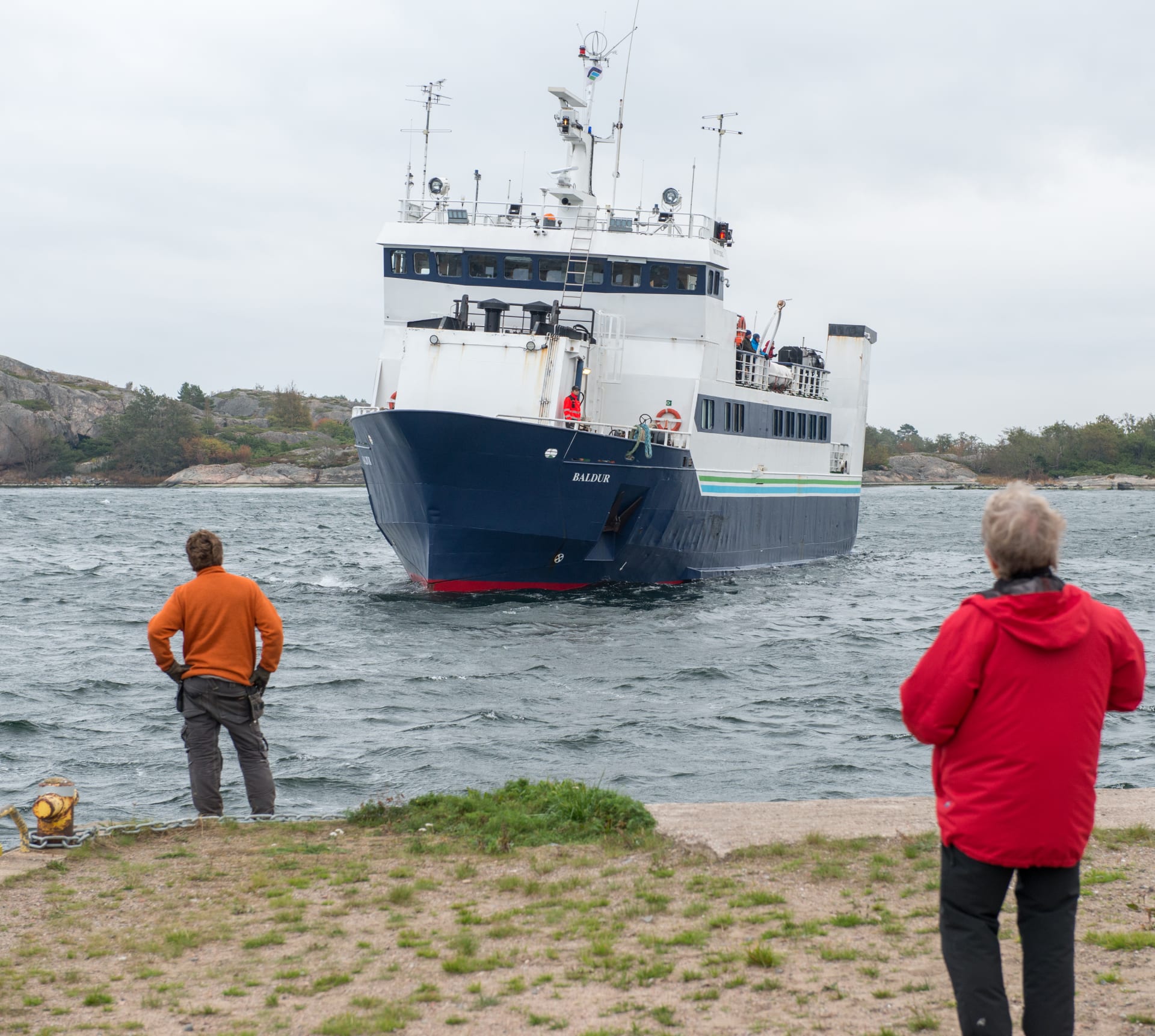 Iso laiva lähestyy laituria. Laiturilla laivaa odottaa kaksi ihmistä.   A big ship approaches the pier. Two people are waiting for the ship at the pier.  Ett stort skepp närmar sig bryggan. Två personer väntar på fartyget vid bryggan.