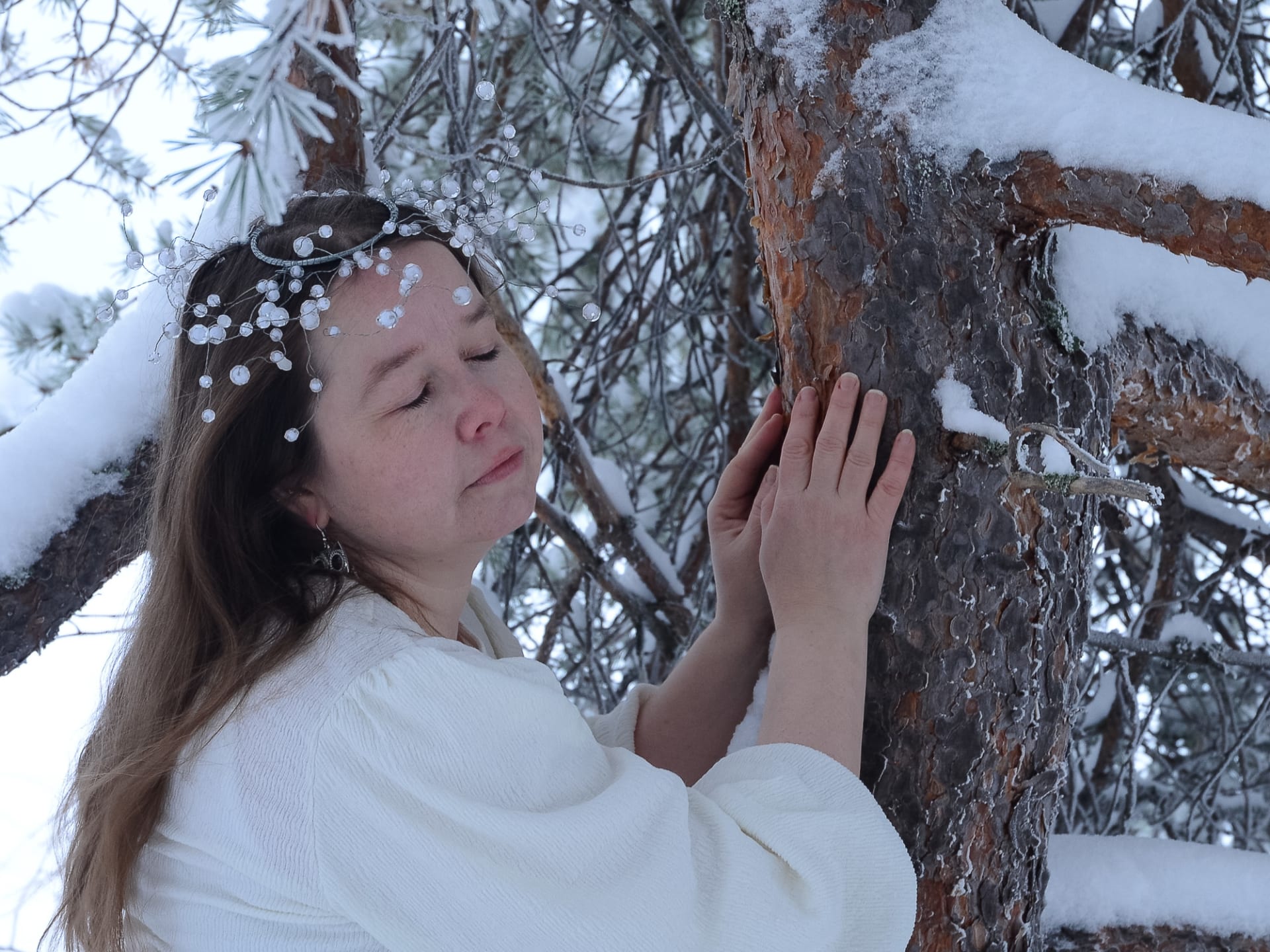 Woman eyes closed leaning into a pine tree.