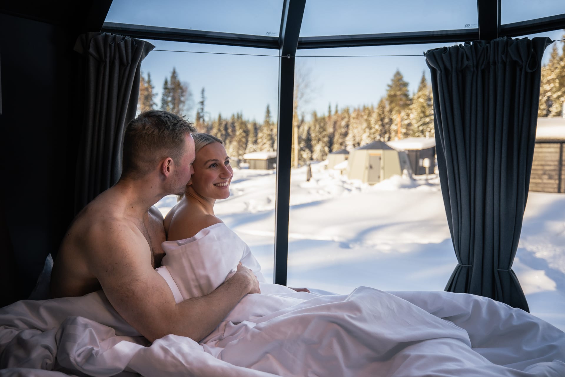 A couple watches the view from inside their Aurora Hut