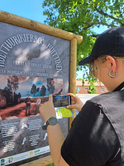 A person scanning QR code on the Kulttuurikierros' signboard.