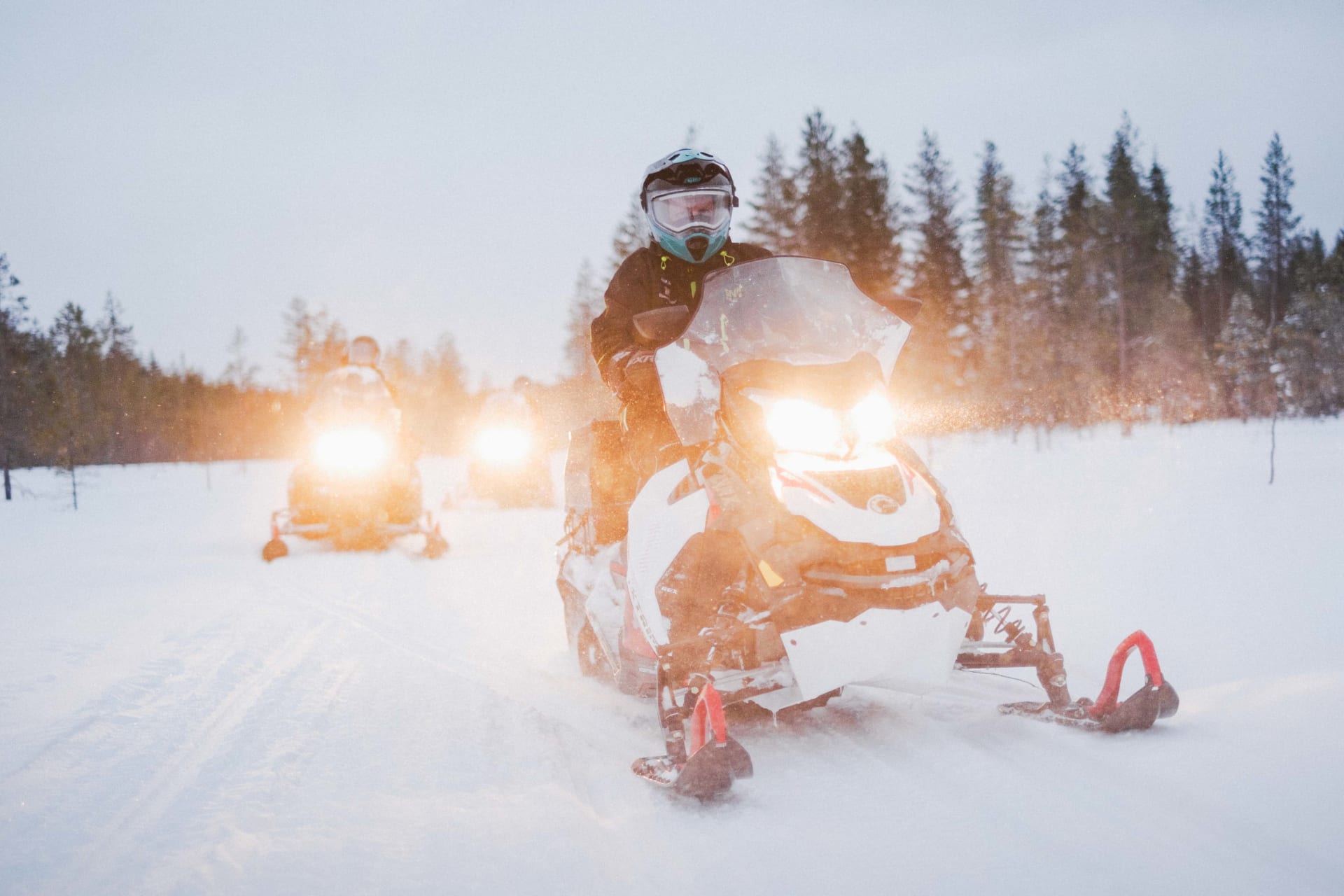 Three snowmobiles driving in the snowy landscape