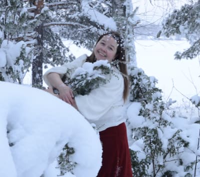 Woman ebracing a juniper bush in a snow-white landscape.
