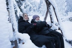 Kaksi muorta naista talviasuissaan istuu kiikussa, maisema on luminen.