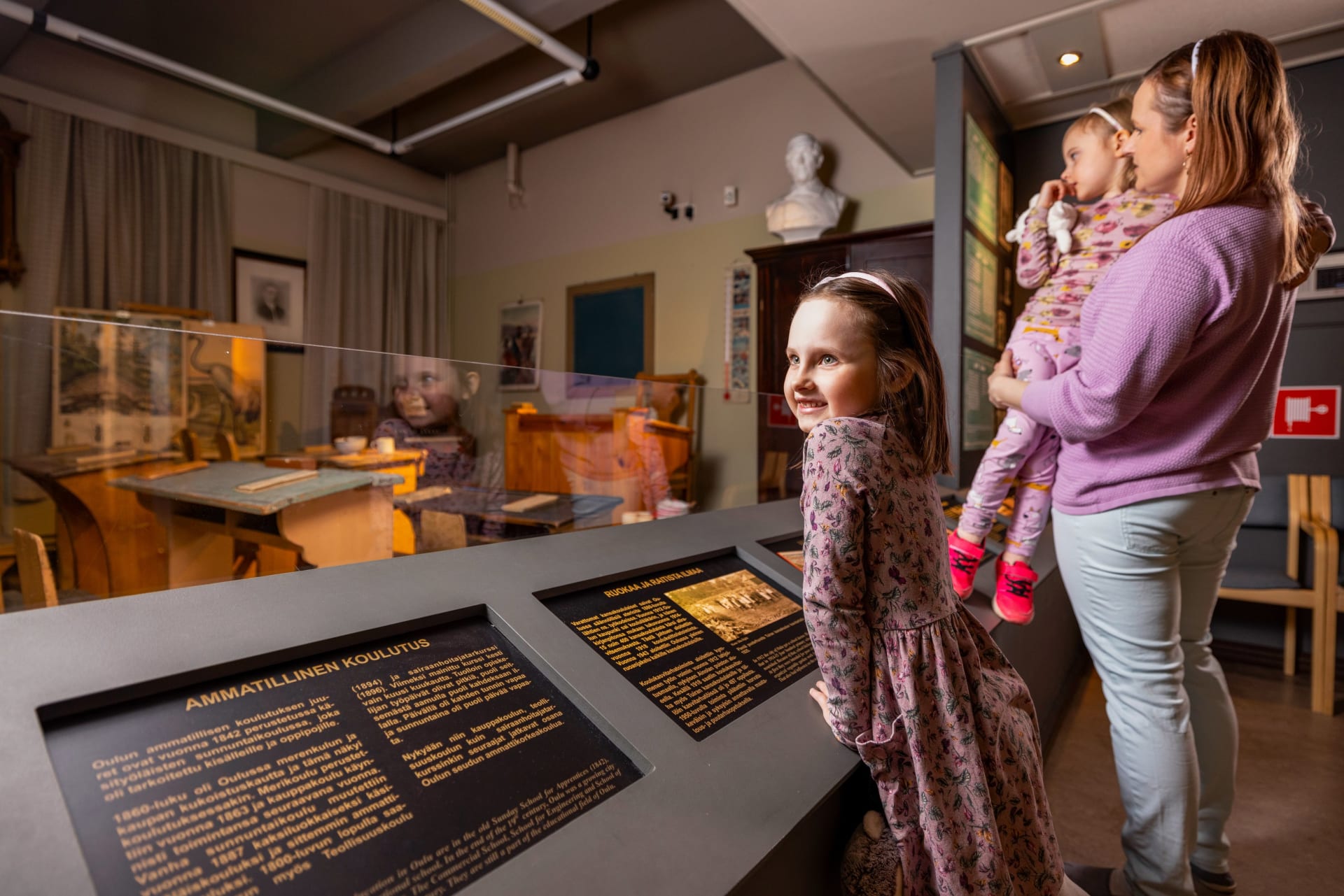 A girl leaning on the museum's signboard. An old time school classroom In the background.