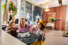 A family dressed in role costumes playing with children’s porcelain tableware.