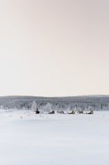 Reindeer sleds move slowly across an open snow-covered landscape at Jänkä, with guests traveling through a wide, quiet winter scene.