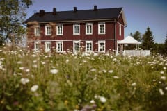 Red two story log house with white framed windows and flower filed in the foreground