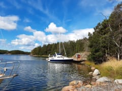 Veneitä kiinnittyneenä laturiin. Väreileivästä merenpinnasta heijastuu veneen peilikuva. Taustalla näkyy havupuumetsää ja pieniä saaria. Sinisellä tavaalla on valkoisia poutapilviä. On kaunis kesäpäivä. Kuva: Kirsi Nikkola.