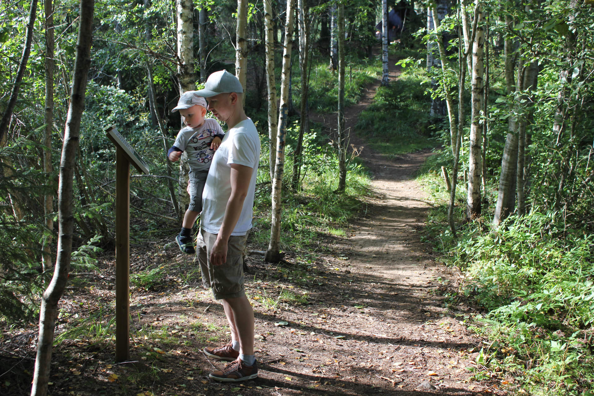 An adult and child are looking at a nature path signboard.