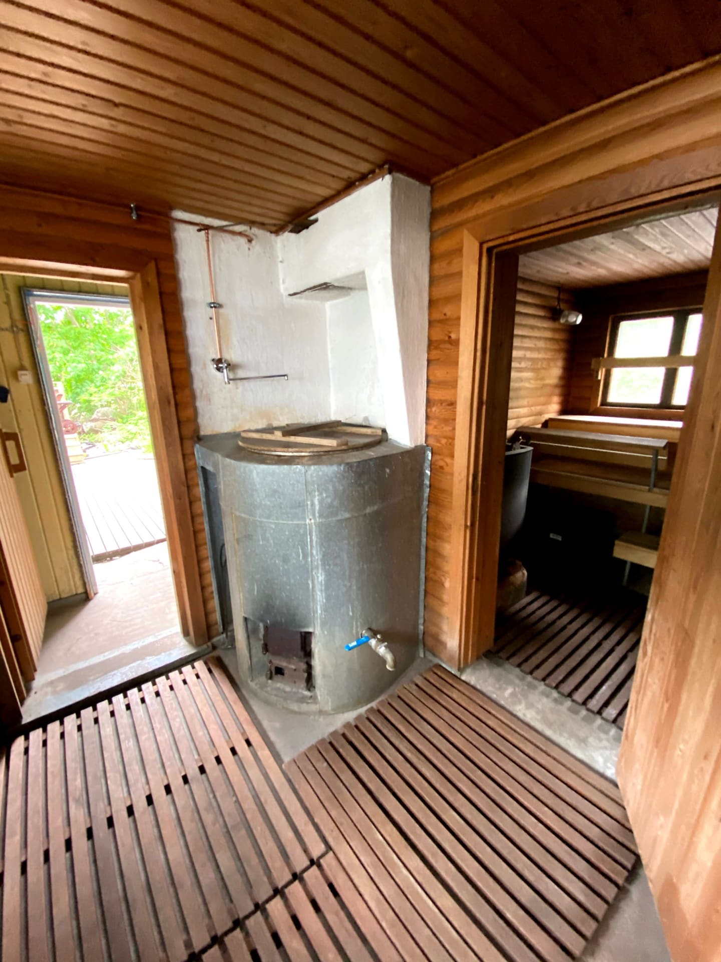 Entrance of a rustic sauna with a water heater in the hallway and a view into the steam room.