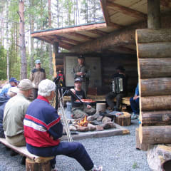 People sitting around the fireplace and grilling sausages in summertime.