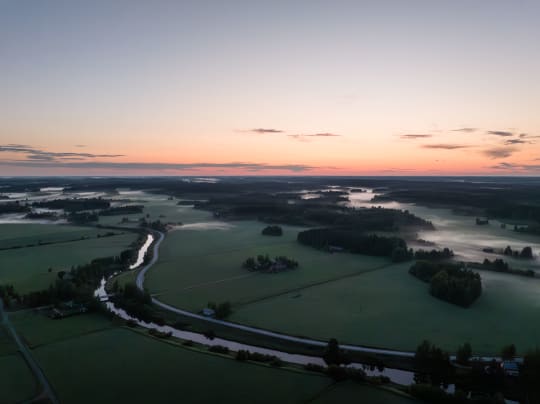 Aerial view of the fields and rivers of Taikayöntie Road with the red sky of sunset in the background.