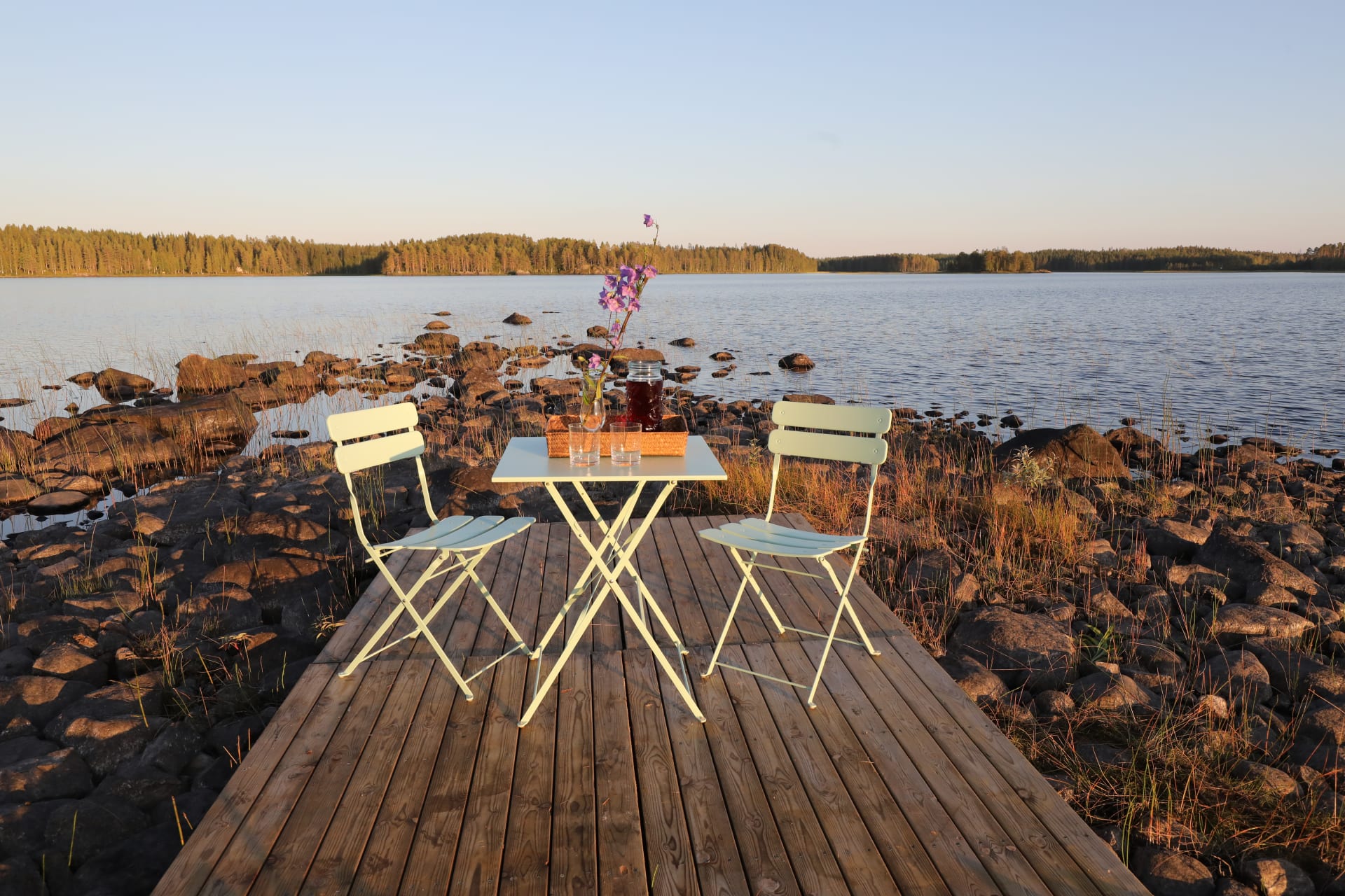 An inviting light furniture group set on a wooden platform at Liukku peak of Lake Korpijärvi, offering a clear view of the lake.