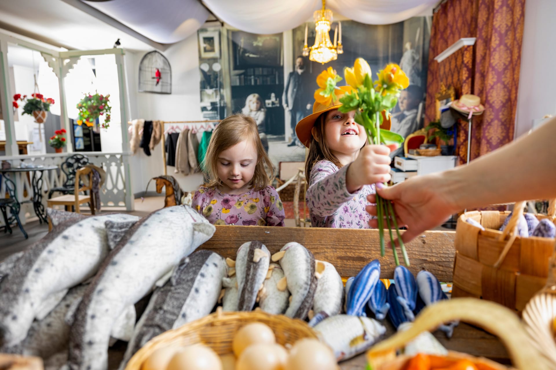 Two girls playing in front of the fish counter. The other girl is holding a bouquet of flowers.