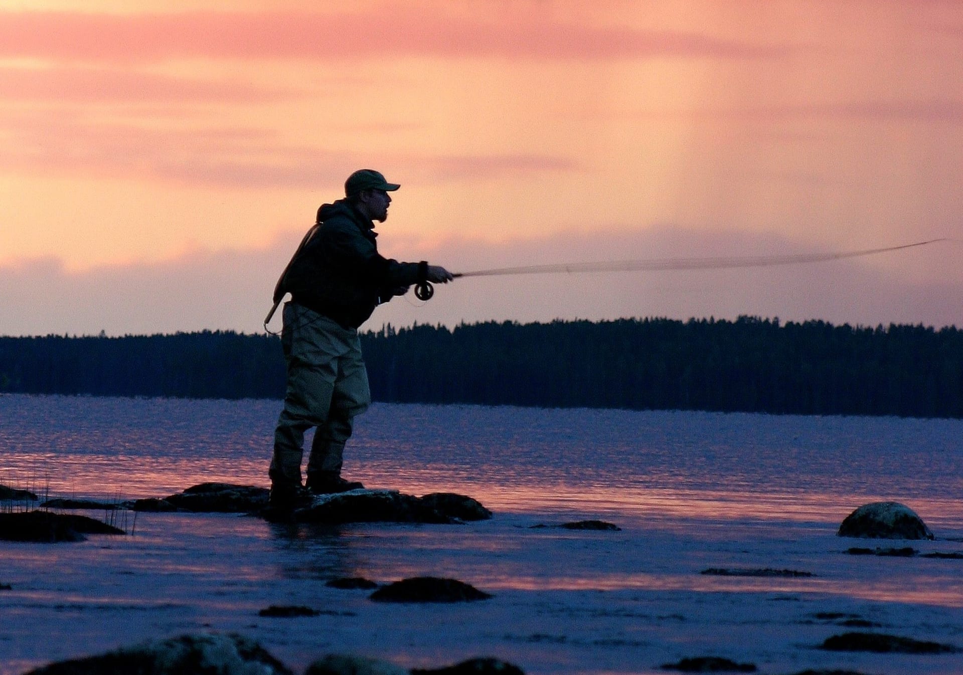 Fly-fishing man against purple sky.