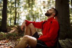 Man sitting and leaning against a tree in the sunny forest