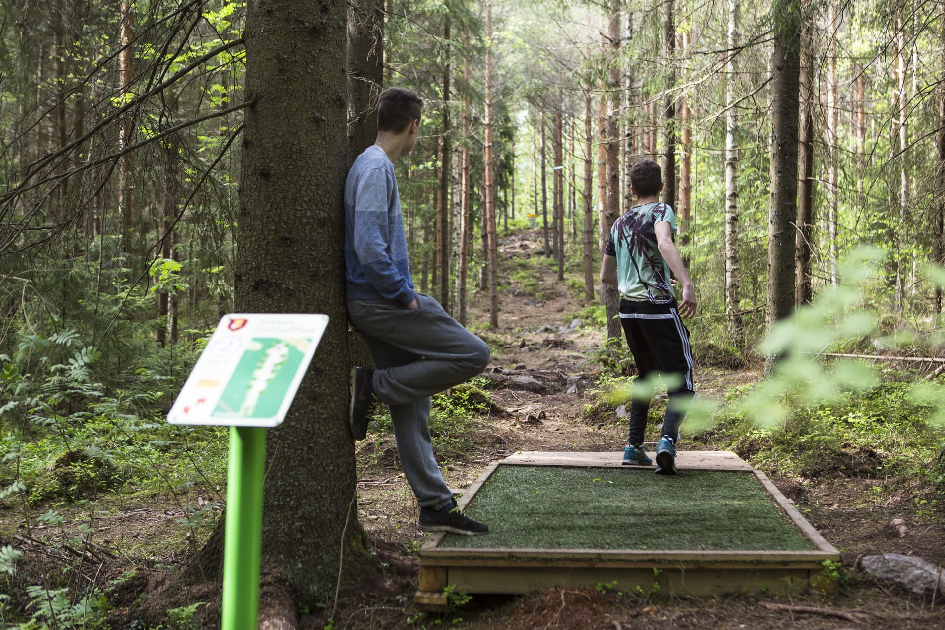 Henkilöitä frisbeegolfradan heittopaikalla