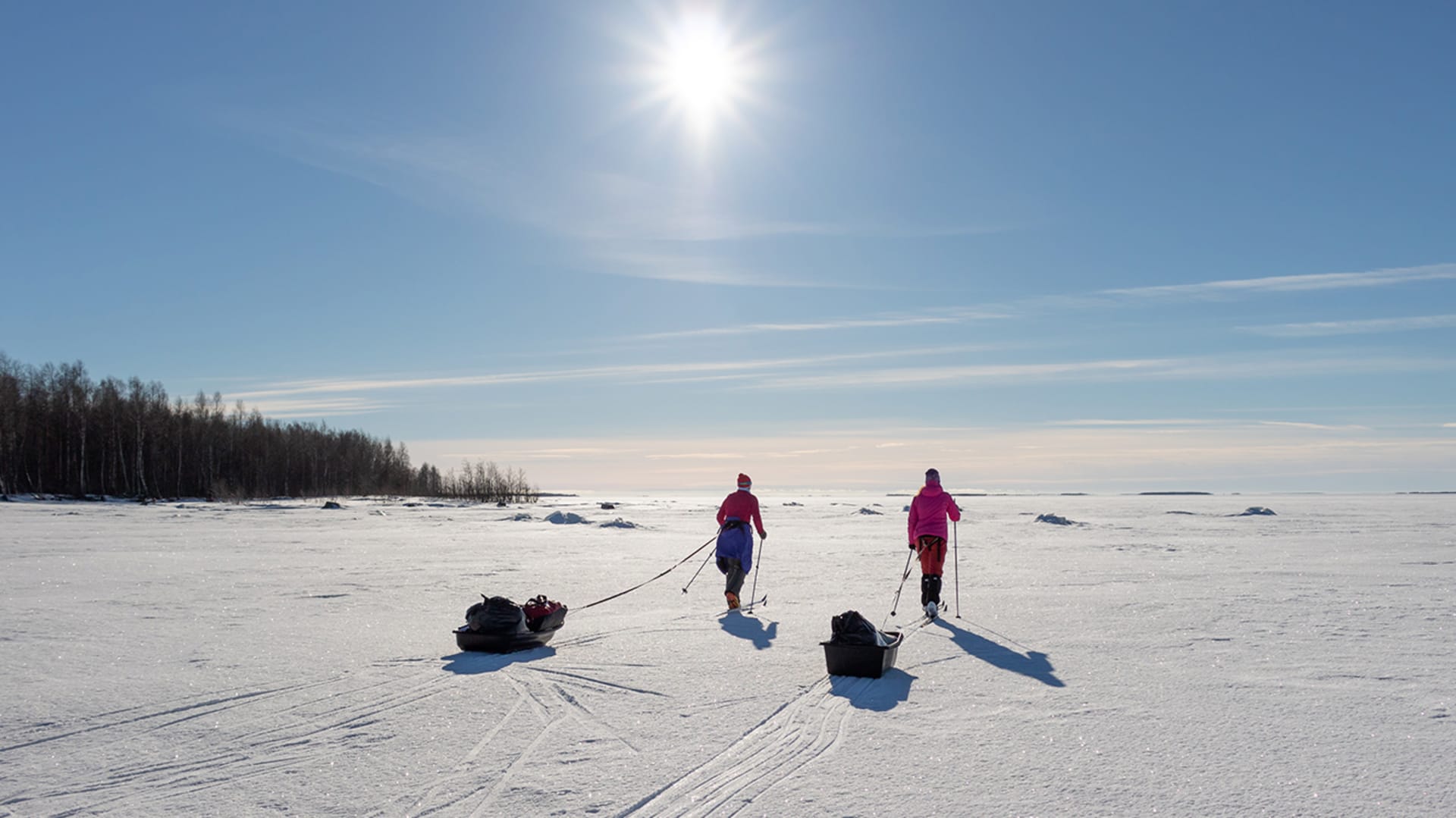 Kaksi hiihtäjää merenjäällä perässään ahkiot. Aurinko paistaa pilvettömältä taivaalta. /  Two skiers on sea ice with packs behind them. The sun shines from a cloudless sky. Kuva: Sini Salmirinne