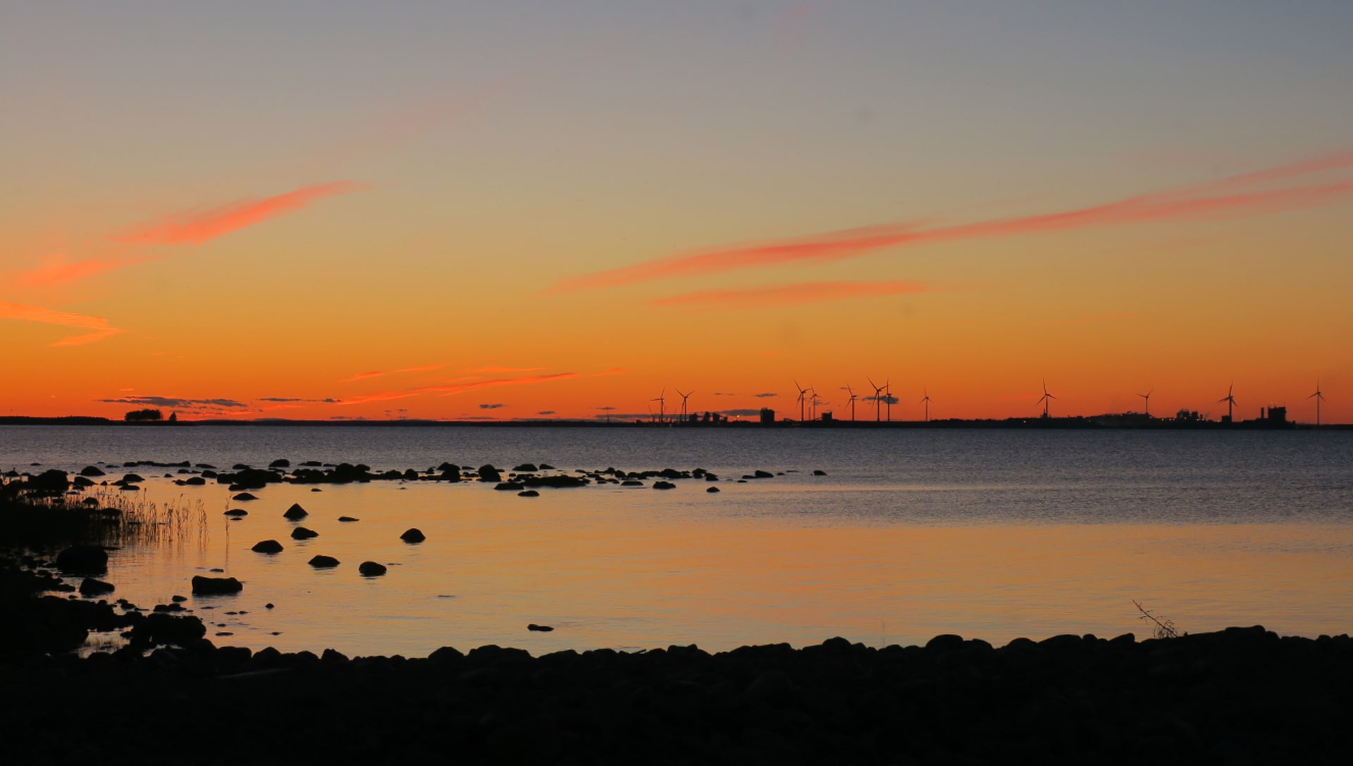 Ilta saaressa. Etualalla kivikkoinen ranta ja horisontissa näkyy tuulimyllyjä. /  An evening on the island. In the foreground is a rocky beach and windmills can be seen on the horizon. Kuva:Ulla Matturi