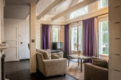 A living room with two sofas, an armchair, a table and a tv and with floor to ceiling windows with a lake view.