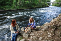 Kaksi henkilöä eväshetkellä kosken rannalla. Kuva: Ulla Keituri