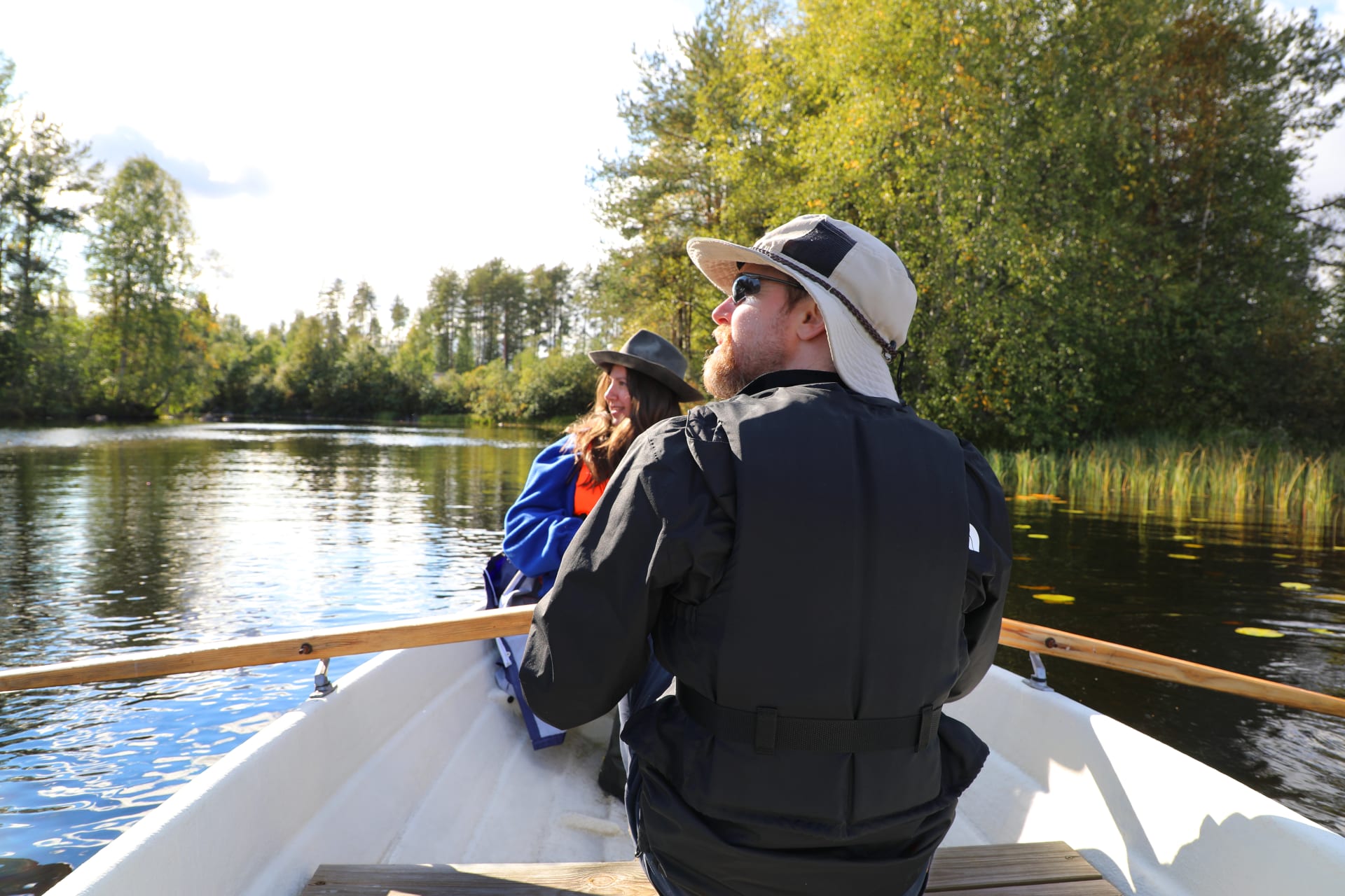 A young couple rowing leisurely across the completely still Lake Korpijärvi on a sunny day.