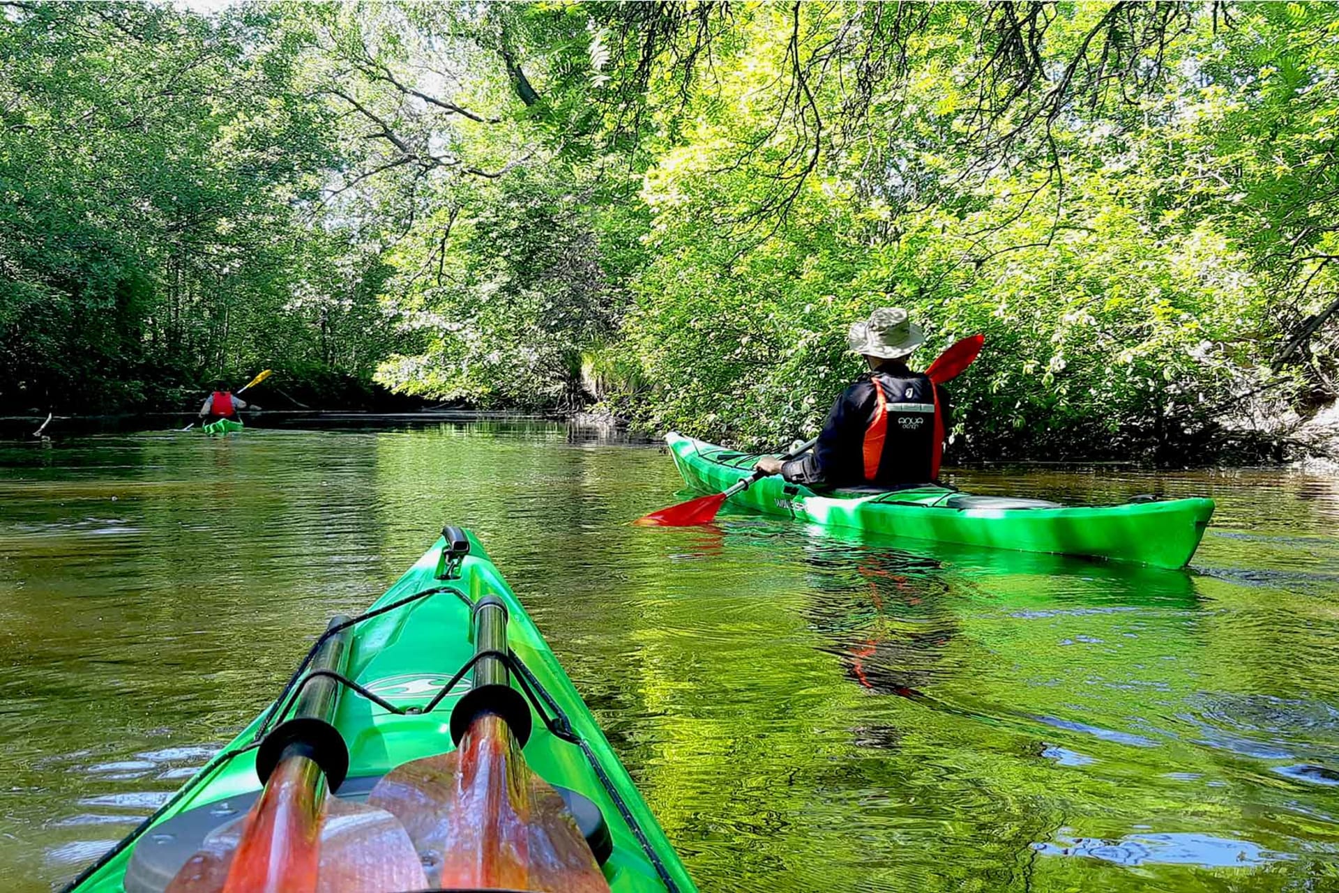 A peak of a green kayak and another person kayaking on a river. 