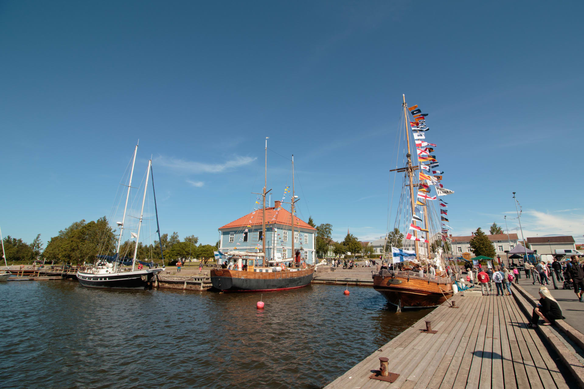 Traditional sailing ships anchored on the shore of the Packhouse museum on a summer day.