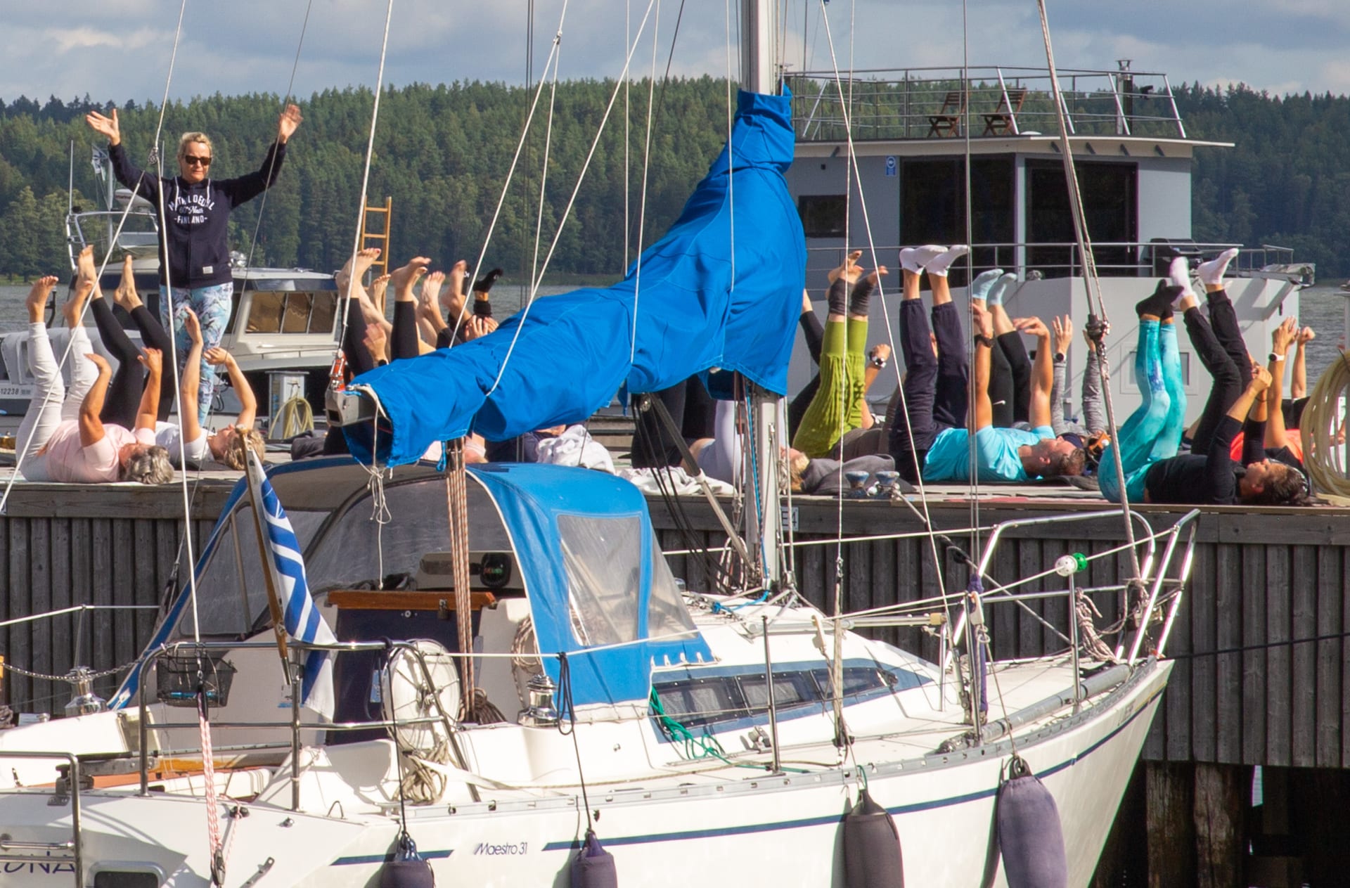 A group is taking part of Yoga Session on the pier next to a sail boat at the pier.