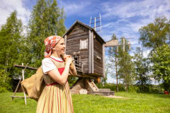 A girl carries a bag of flour in front of a wooden windmill.